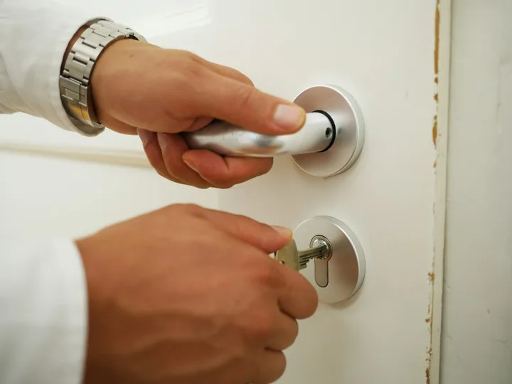 Chaveiro residencial em Varginha: mão na maçaneta e chave na fechadura da porta de casa
